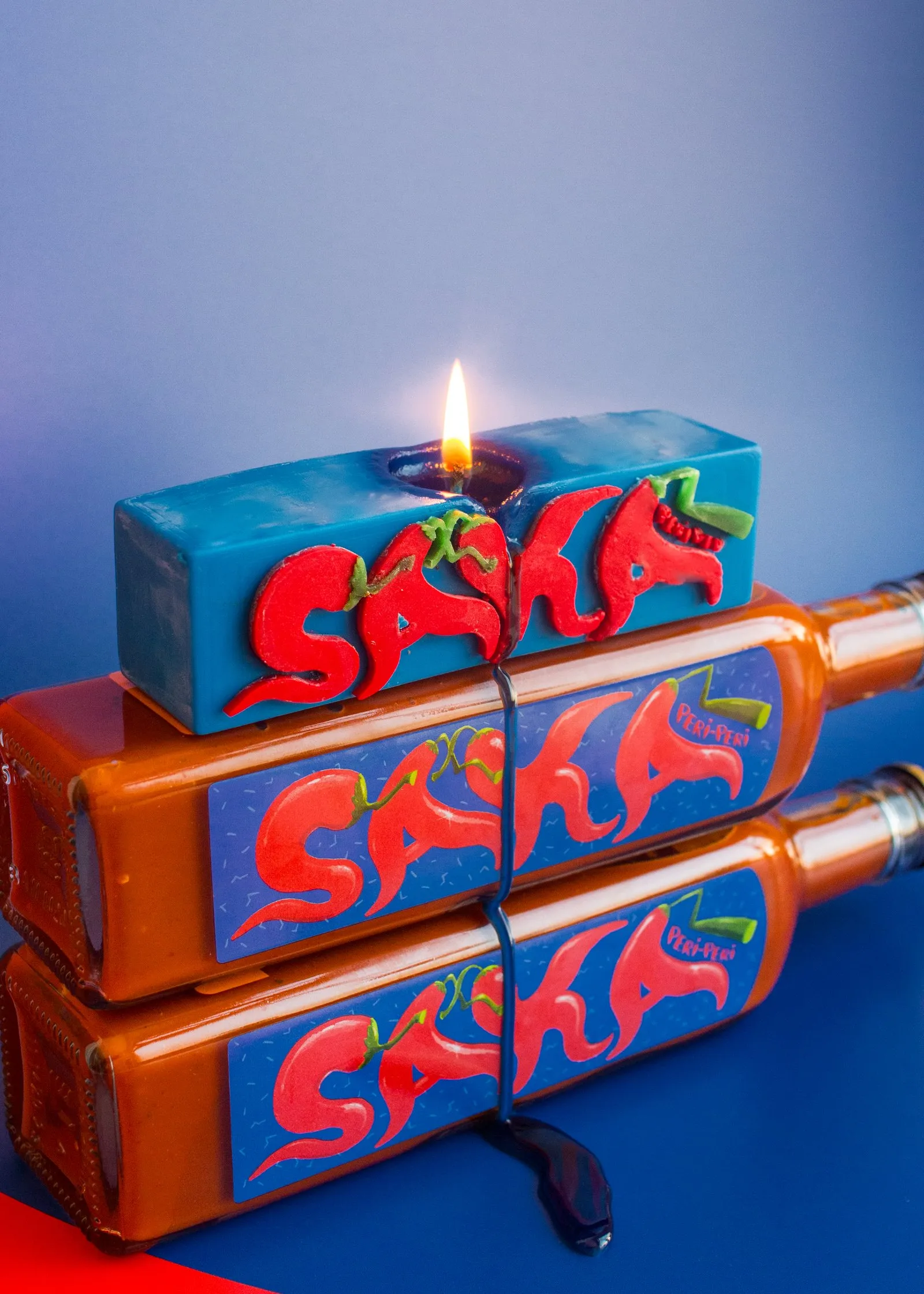 The Nata x Nando's PERi-PERi Saka candles, stacked, with the top candle lit