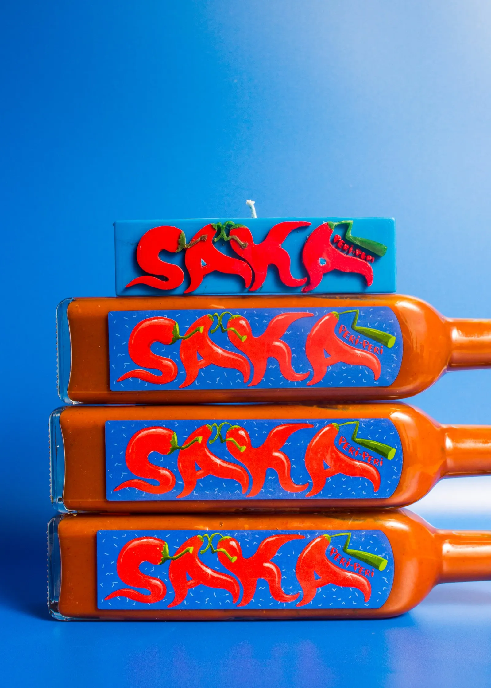 Nata x Nando's PERi-PERi Saka candles stacked against a blue backdrop