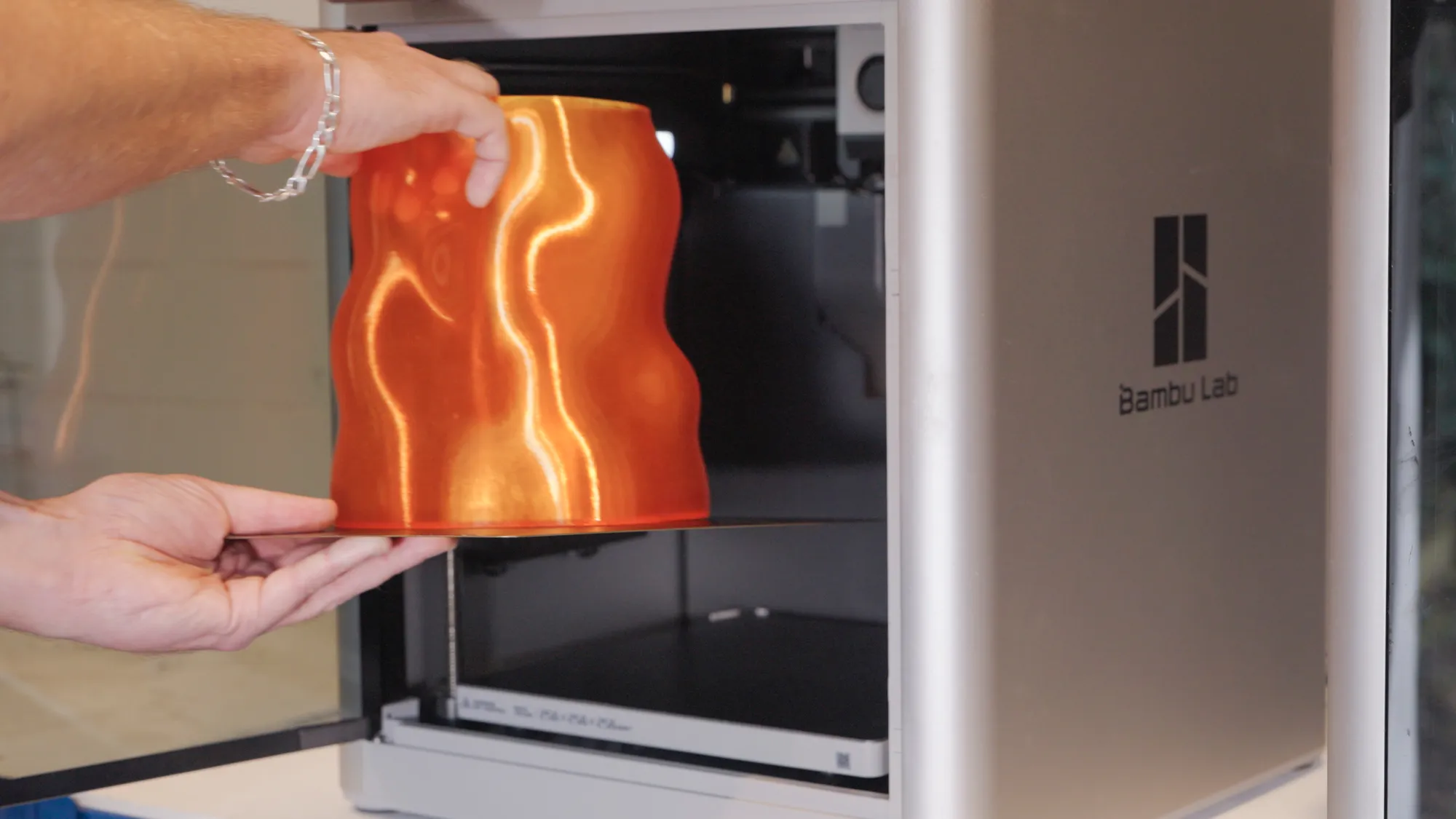 An orange vase lifted off the build plate of a Bambu Lab X1 Carbon printer