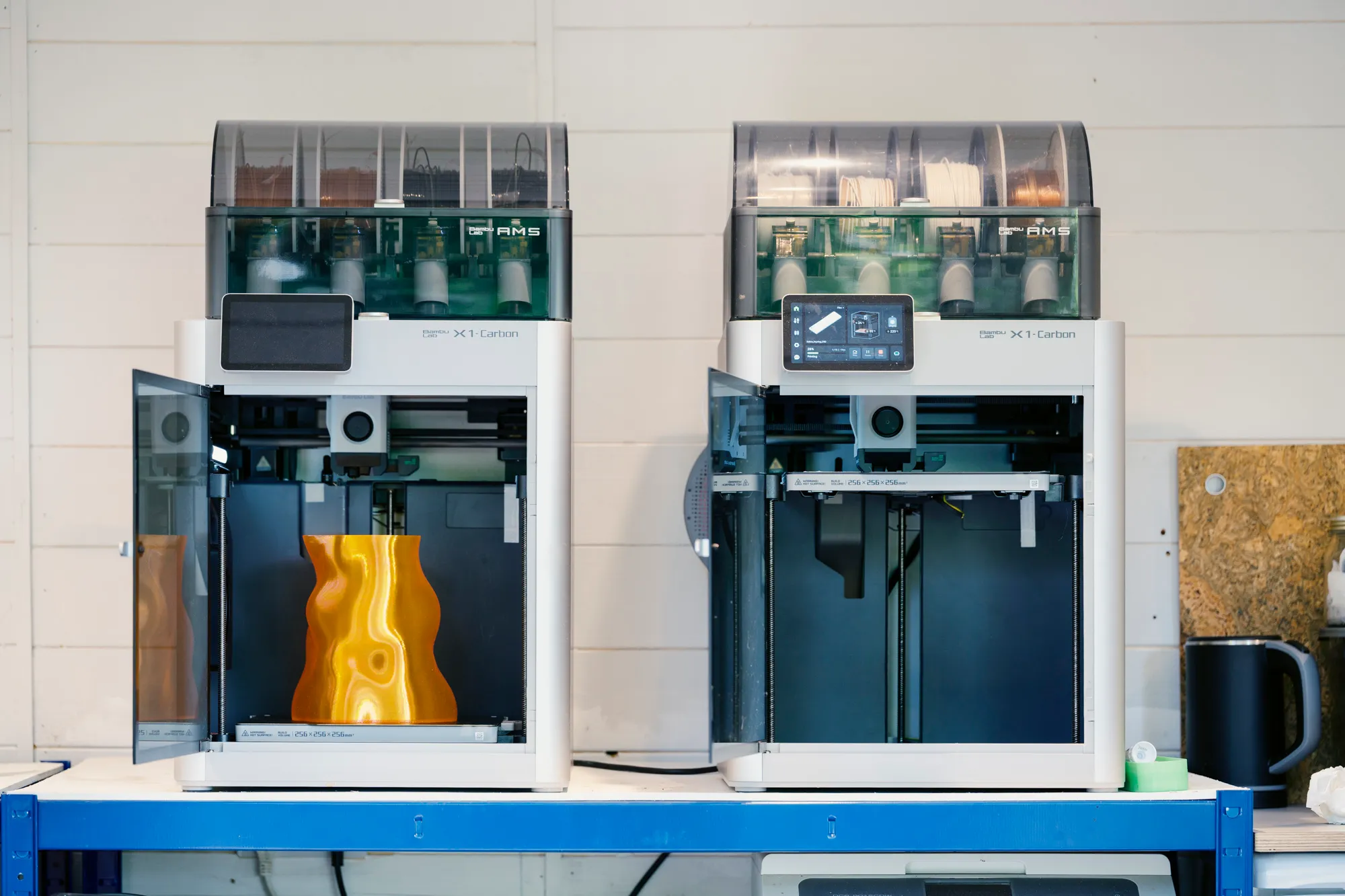 Two Bambu Lab X1 Carbon printers in the Spike TM studio, one printing an orange vase