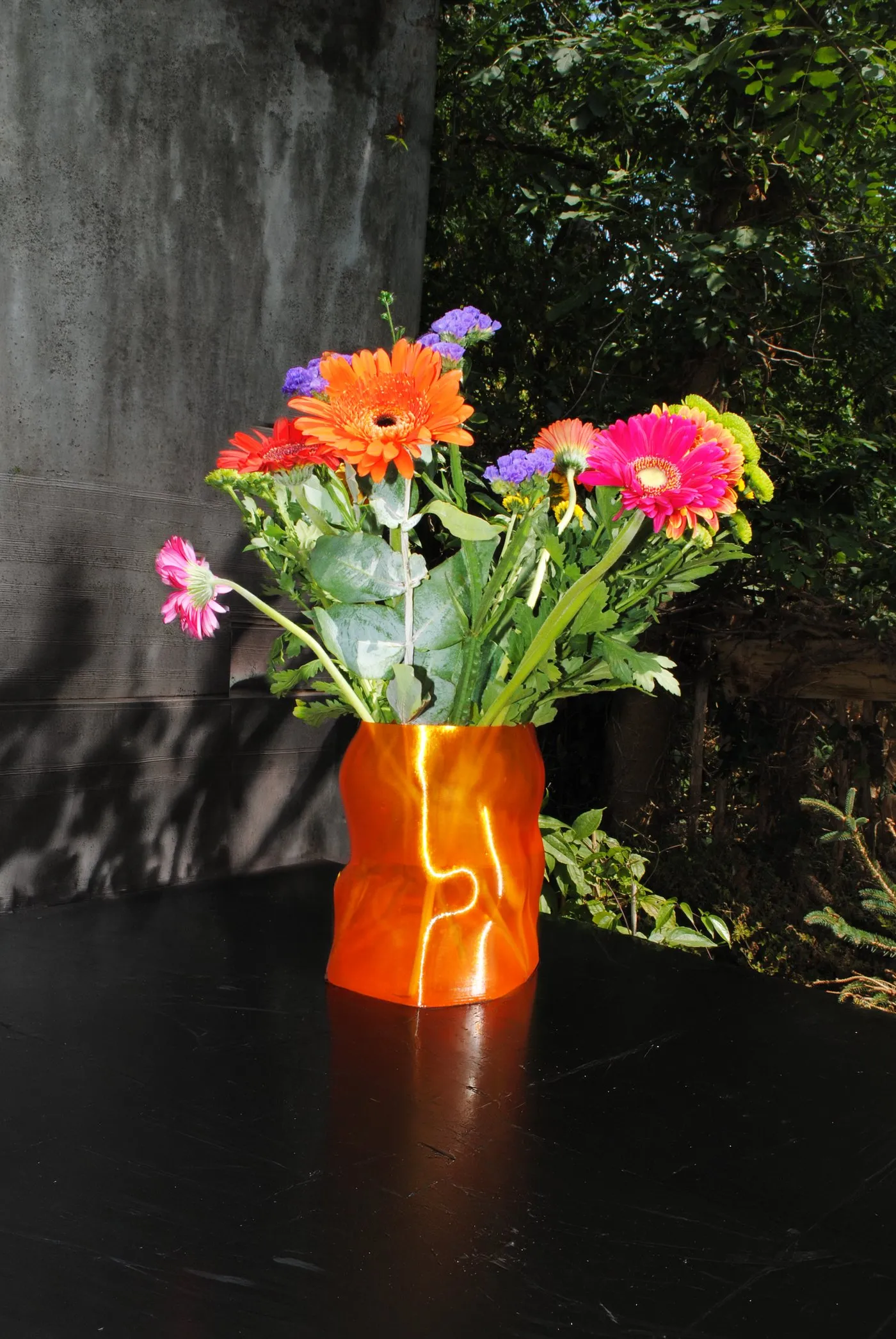 Peski vase in Tangerine with gerberas on a dark table outdoors